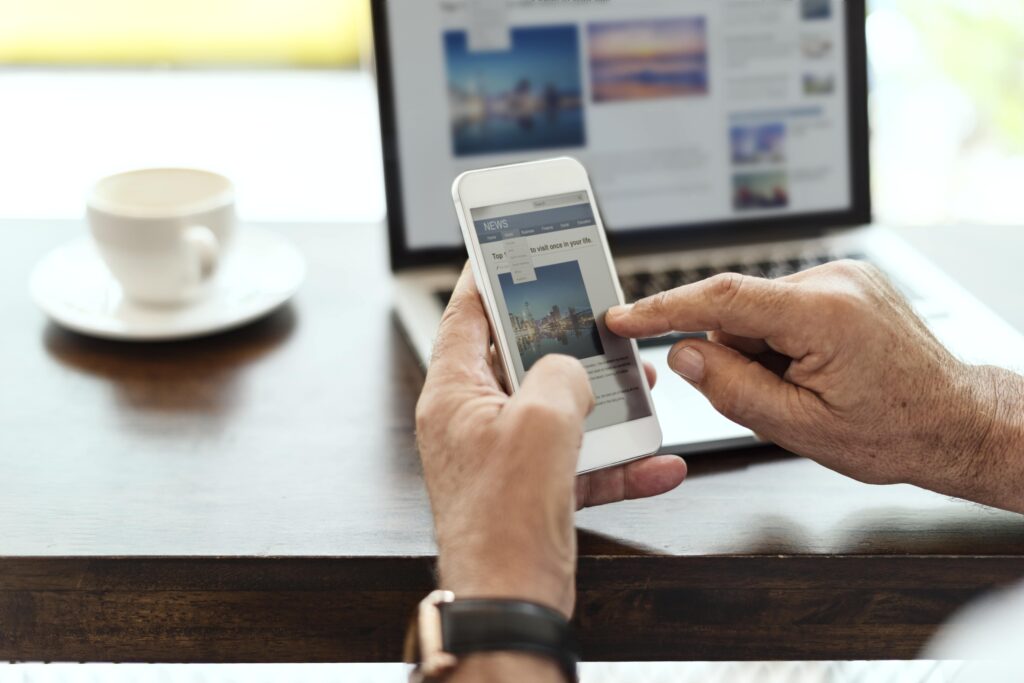 Homem vendo anúncio online no celular e com a tela de um site de viagem no fundo do notebook